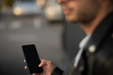 Closeup shot of an unrecognizable young man holding mobile phone in hand, blurred background