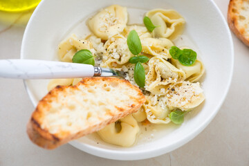 Tortellini in bouillon served with grated parmesan and fresh basil in a white bowl, middle closeup, selective focus