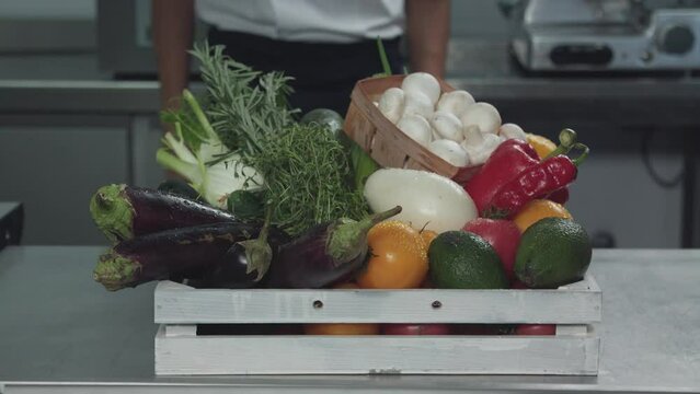 Cook puts a box with vegetables, greens and mushrooms on the table. A man carries a box with vegetables, greens and mushrooms and put it on the table of restaurant cuisine