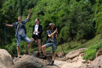 Young man hiker with backpack and trekking poles with a young man helping to pull him up to stand on the rock