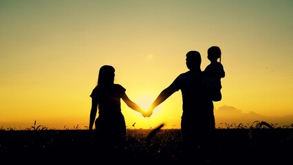 Naklejka na ściany i meble Mom dad child walk hand in hand. Happy family of farmers with child, are walking on wheat field. Slow motion. Mother father, little daughter enjoying nature together outdoor. People travel. Silhouette