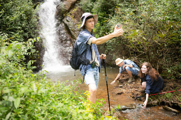 Naklejka na ściany i meble Man and woman hikers taking pictures of themselves at the waterfall in forest