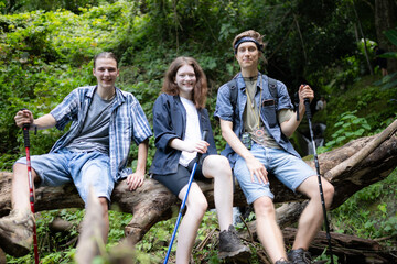 Group of friends with backpacks and sticks sitting on a fallen tree, Take a break during the hike