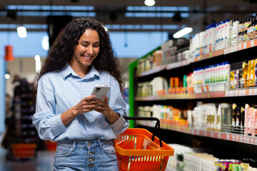 A young Latin American woman is shopping in a supermarket among the shelves with goods, a woman...