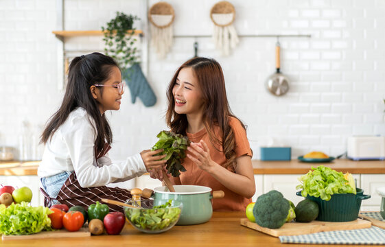 Portrait of enjoy happy love asian family mother with little asian girl daughter child help cooking food healthy eat with fresh vegetable testing smell soup in a pot with spoon.help mommy in kitchen