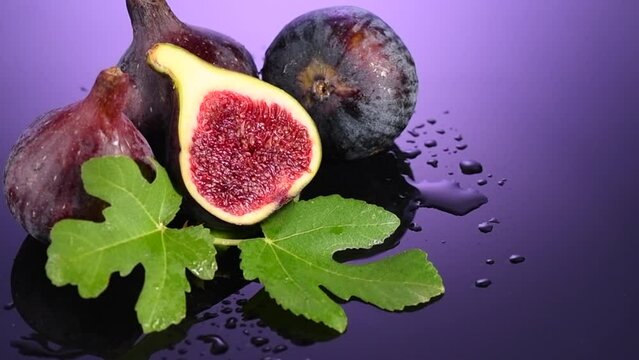 Fig fruits. Ripe sweet figs fruit with leaves close up, on purple, violet background. Water drops. Rotating fresh exotic fruits. Slow motion. 