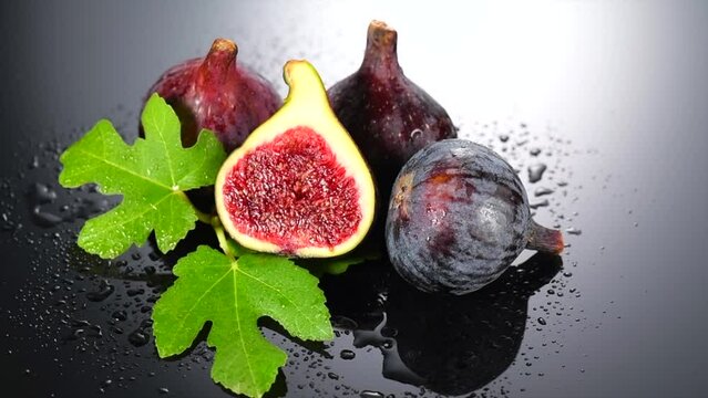 Fig fruits. Ripe sweet figs fruit with leaves close up, on dark grey background. Water drops. Rotating fresh exotic fruits. Slow motion. 