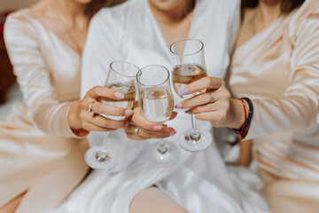 Smiling bride and her friends are sitting on the bed in the bedroom and drinking champagne