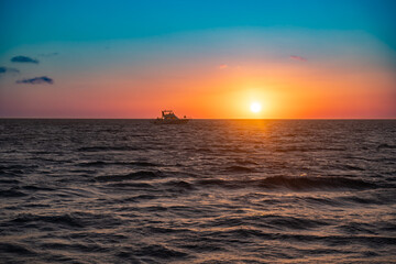 Beautiful nature scene of colorful sunset over ocean with boat on horizon