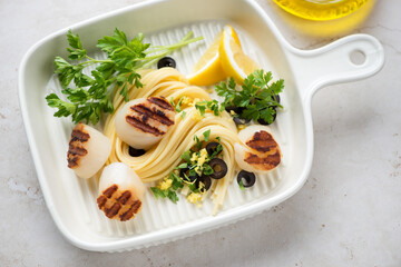 Grilled scallops with spaghetti, lemon zest and parsley in a beige serving tray, horizontal shot