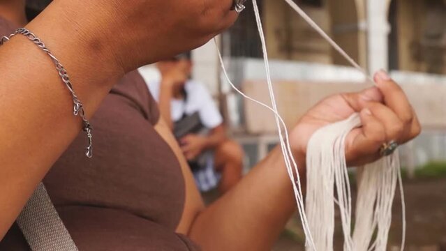 Filipino woman belonging to marginal earners prepares cotton strings thread to make candle wick at the side of the street