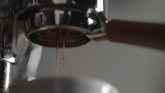 Slow motion low angle shot of espresso extraction from naked portafilter into white cup