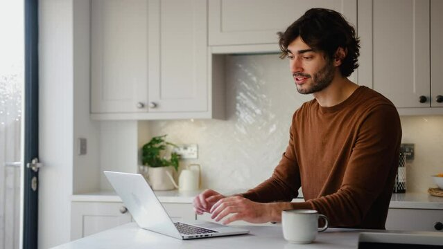 Young man working from home on laptop sitting at kitchen counter - shot in slow motion