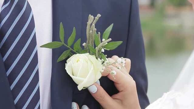 Woman's hands attach a white rose to the man's jacket. Probably, the man is a groom