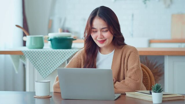 Happy positive young asian woman enjoying online communication at home, Female using wifi while video conferencing with friend, sitting in front of open laptop, smiling and waving hand, saying hi