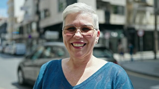 Middle age grey-haired woman wearing sunglasses smiling at street