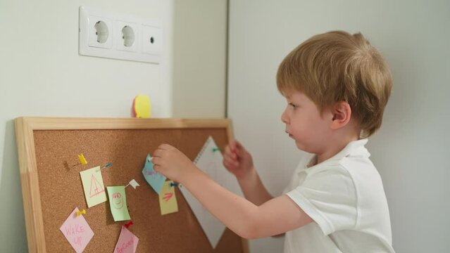 Toddler boy attaches note to board playing with stationery