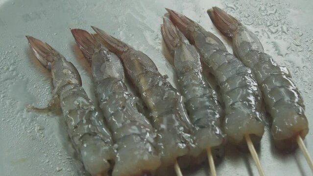 Sprinkle the prawns with salt. Pebbles of salt are falling on the raw prawns in slow-motion.