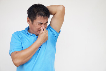 Asian man is checking his odor underarm, close his nose with hand, feel disgusted the body strong smell. Concept , health problem. Unpleasant body odor , smell nasty reaction. Negative emotion.       