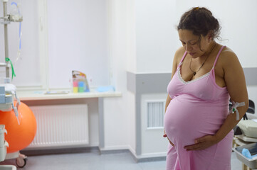 Pregnant woman birthing mother with painful contraction, touching belly and looking down....