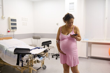 Pregnant woman in hospital ward, counts her contractions using mobile app in her smartphone, during...