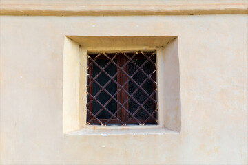 Fototapeta na wymiar Vecchia piccola finestra quadrata chiusa con sbarre metalliche su muro di vecchio edificio.