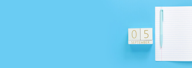 05 September. Wooden calendar on a blue background with an open notepad, top view. Back to school. Perpetual calendar, notebook and pen. Mock up