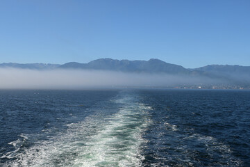 Ship's wake in Juan de Fuca Strait with Port Angeles, Washington, Olympic Mountains and fog bank in background on sunny summer morning.