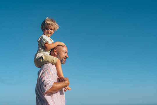 dad carries his son on his shoulders against the sky