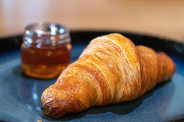 Fresh croissant with honey on plate.
