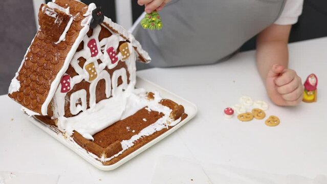 siblings boys doing with granny gingerbread christmas house.preschooler child wearing toque chef  hat,apron,mixing cream,licking from wires beaters.toddler with tree headband,modern kitchen 4k