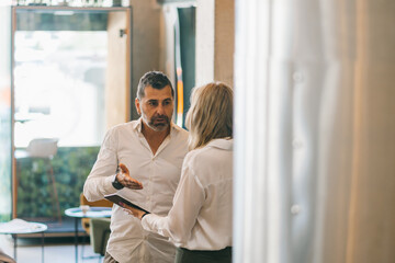 Handsome middle-aged company leader giving some tasks to his blonde secretary before he keeps working with the project and the rest of the team