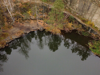 Picturesque aerial view of landscape with emerald lake and rocks in the middle of a coniferous autumn forest in Korostyshiv granite quarry, Zhytomyr district, northern Ukraine. Zhytomyr canyon