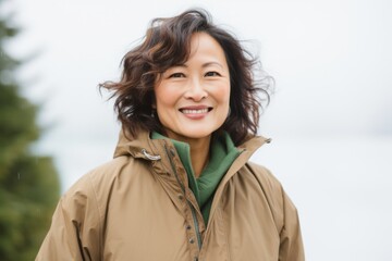 Lifestyle portrait of a Chinese woman in her 50s in a white background wearing a warm parka
