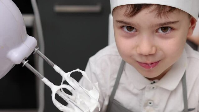 siblings boys doing with granny gingerbread christmas house.preschooler child wearing toque chef  hat,apron,mixing cream,licking from wires beaters.toddler with tree headband,modern kitchen 4k