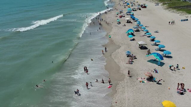 aerial footage of a gorgeous summer landscape at the beach with people relaxing in the sand under colorful umbrellas with ocean water, waves in Carolina Beach North Carolina USA