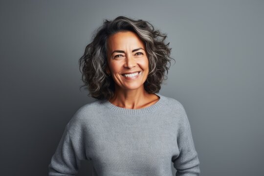 Lifestyle Portrait Of A Brazilian Woman In Her 50s In A Gray Background Wearing A Cozy Sweater