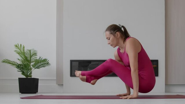 Young female performs acrobatic exercises hands on red mat in stodio, Flexible woman in sportswear doing splits in fashion look on sunny day at home
