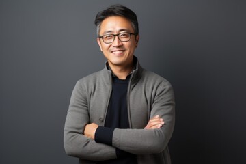 Fototapeta premium Portrait of a happy asian man with arms crossed against grey background