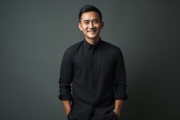 Fototapeta premium Portrait of a happy young asian man in black shirt against grey background