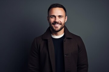 Fototapeta premium Portrait of a handsome young man in a jacket smiling at the camera while standing against grey background