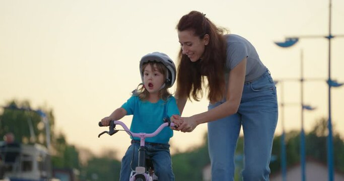 Mom teaches daughter to ride a bike. Happy family childhood dream concept. Mother and little daughter learn to ride a bike in the park. Happy family goes in for sports outdoors sunlight