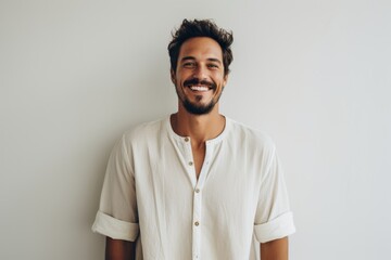 Fototapeta premium Lifestyle portrait of a Brazilian man in his 30s in a minimalist or empty room background wearing a simple tunic