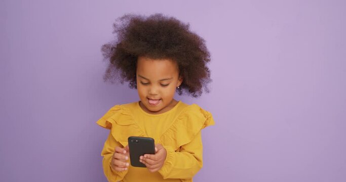 smiling pretty little African girl holdong her parents smart phone, enjoying surfing browsing the internet, Slow motion, child is addicted to mobile phone, generation M