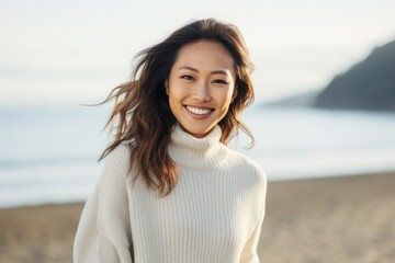 Portrait of smiling asian woman in sweater looking at camera on beach
