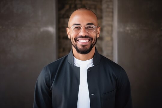 Portrait of a handsome young man in a black jacket and glasses smiling at the camera.