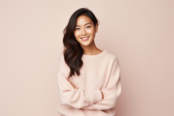 Fototapeta premium Portrait of a smiling young asian woman with arms folded over pink background