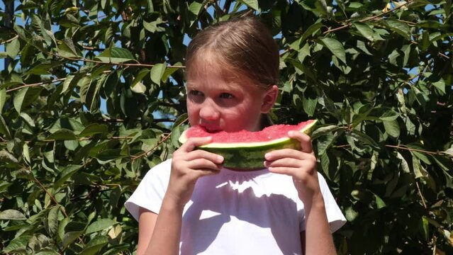 Happy little girl eats watermelon in garden sunny summer day on green tree background
