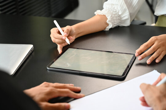 Close up image of businesswoman working with a digital tablet and showing it to someone who sitting opposite, discussing with customers, signing agreement documents.