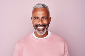 Portrait of a handsome mature man smiling at the camera while standing against pink background